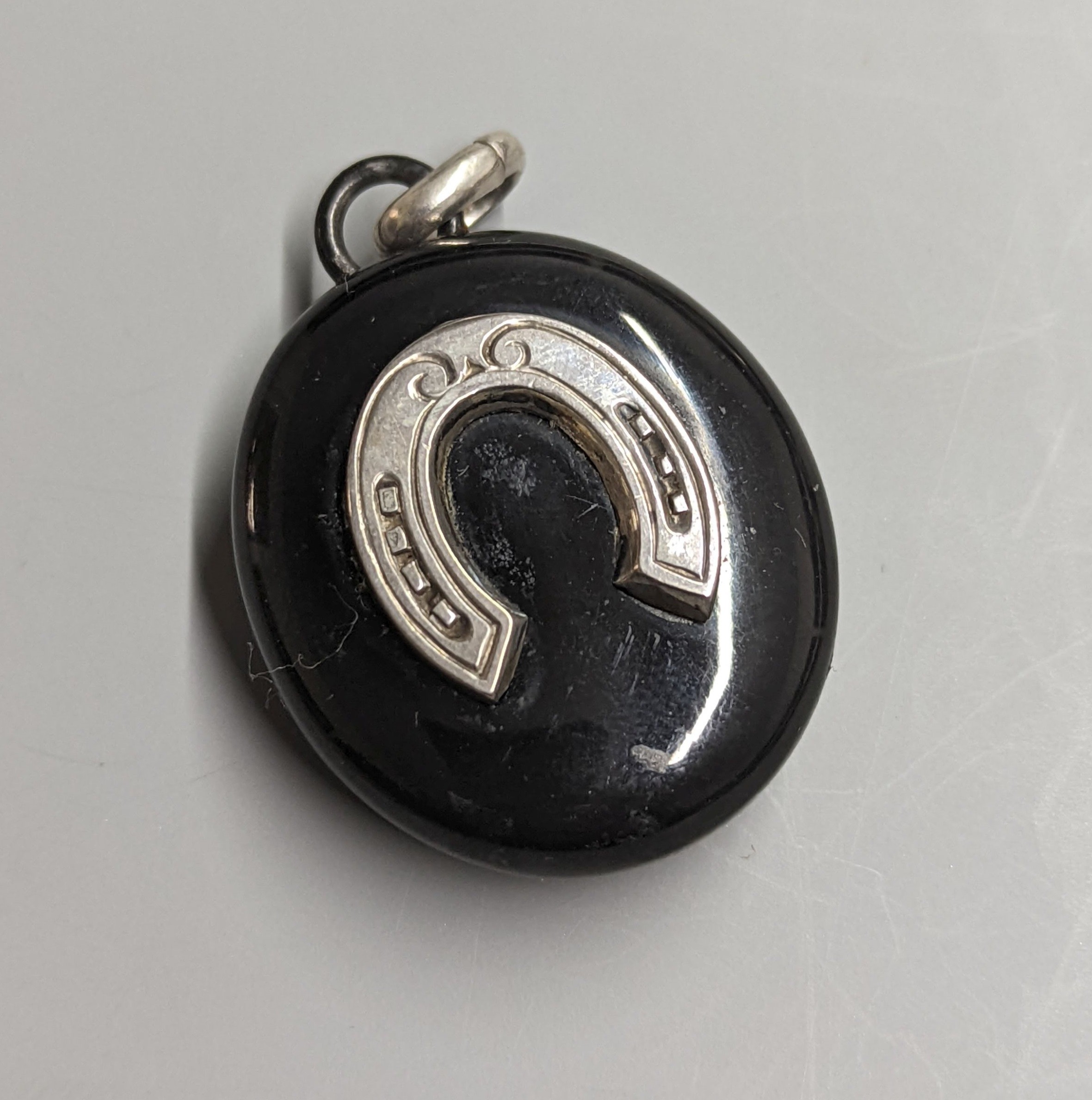 A late Victorian white metal and black enamelled oval mourning locket, with horseshoe applique and glazed back, 42mm.